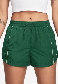 Πράσινες αθλητικές βερμούδες κατασκευασμένες από ελαφρύ ύφασμα, με ελαστική ζώνη μέσης, κορδόνι και λευκές πλευρικές λεπτομέρειες για αντίθεση.
