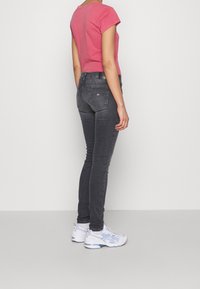 Jeans ajustados gris oscuro con bolsillos traseros, combinados con una camiseta de manga corta rosa y zapatillas blancas con detalles en azul.