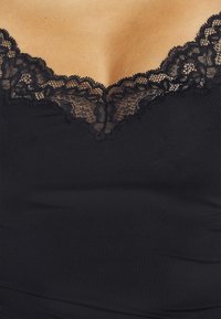 Black camisole featuring a scalloped lace trim along the neckline. Made of smooth fabric with a fitted shape.