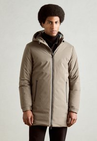 Parka beige con capucha, cierre frontal, dos bolsillos laterales y puños elásticos. Material suave con acabado mate.
