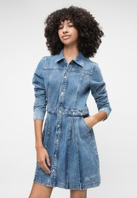 Φόρεμα τζιν με αυστηρή εφαρμογή, μακριά μανίκια, κουμπωτή μπροστά, σφιχτή μέση και πλαϊνές τσέπες. Ανοιχτό μπλε απόχρωση με λεπτομέρεια λογότυπου.