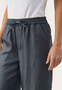 Ciemnoszare, pomarszczone spodnie z materiału z elastycznym paskiem i sznurkiem do wiązania. Widoczne boczne kieszenie, zestawione z białym, prążkowanym topem.