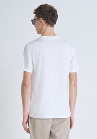Camiseta de algodón blanca de manga corta, con cuello redondo y una textura suave, combinada con pantalones beiges. Vista trasera visible.