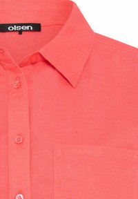 Korallenfarbens Hemd mit Knöpfen und spitzem Kragen, Brusttasche und passenden Knöpfen; aus leichtem Stoff mit strukturierter Oberfläche.