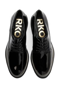 Zapatos de charol negros con cordones y un acabado brillante, que presentan un logo dorado en las plantillas y costuras en contraste a lo largo de la suela.