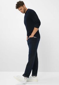 Marineblauwe gebreide trui met ronde hals en geribde manchetten, gecombineerd met donkere jeans en witte sneakers. De jeans hebben zakken en een slim fit.