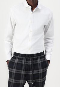 Witte lange mouwen button-up shirt gecombineerd met zwart en grijs geruite elastische broek met tailleband, voorzien van een trekkoord en zijzakken.