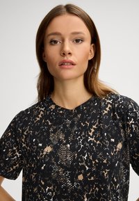 Svart t-shirt med korta ärmar och leopardmönster i beige och vita nyanser. Tillverkad av mjukt material med avslappnad passform.