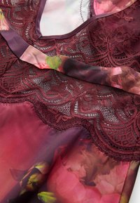 Bordeaux bloemenkant top met een doorzichtige stoffen overlay, met een delicate bloemenpatroon en textuurkant details.