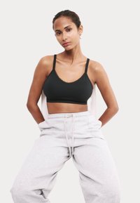 Svart bralette med tunna band och vågiga kanter, matchad med ljusgrå sweatpants, mot en neutral bakgrund.