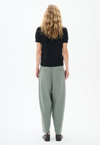 Top nero a maniche corte abbinato a pantaloni felpati leggeri e larghi di colore verde chiaro. L'outfit presenta una texture morbida e una silhouette casual con tasche.