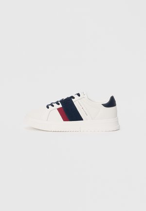Witte sneaker met marineblauwe en bordeauxrode strepen, bovenwerk van stof, rubberen zool, ronde neus en donkerblauwe veters. Minimalistisch ontwerp en branding.