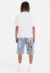 Camiseta de algodón blanca con cuello redondo. Pantalones cortos de mezclilla azul claro con un diseño bordado colorido que incluye una calavera y texto.