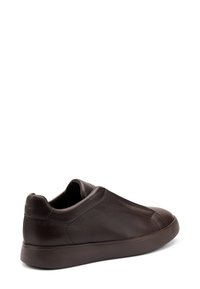 Sneaker in pelle marrone, senza lacci, con punta arrotondata, texture liscia e cuciture ton sur ton. Presenta una suola in gomma e un branding minimale sul tallone.