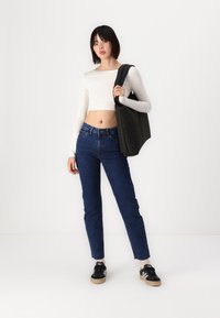 Top corto de manga larga blanco, bolso negro ajustado, jeans de tiro alto azules, zapatillas negras con rayas blancas y calcetines beige.