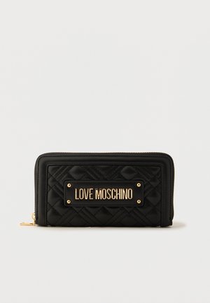 Melnas kviltētas maks ar rāvējslēdzēju apkārt, ar zelta plāksnīti "LOVE MOSCHINO" centrā priekšpusē, uz vienkārša fona.