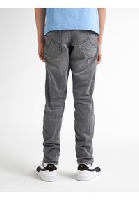 Jeans de mezclilla gris con un corte ajustado, que presentan bolsillos traseros curvados y costuras minimalistas, combinados con zapatillas negras y blancas.