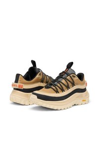 Beige och svarta vandringsskor med ett texturerat ovandel, tjocka grå snören och en klumpig vit sula med orange och grå accenter.