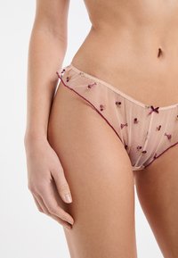 Lingerie in tulle rosa trasparente con motivi floreali ricamati in bordeaux e giallo. Presenta un bordo arricciato e un piccolo fiocco decorativo.