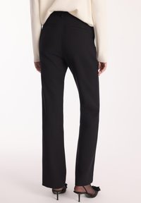 Czarne dopasowane spodnie z prostymi nogawkami, o gładkiej fakturze i dwóch tylnych kieszeniach. Noszone z czarnymi szpilkami.
