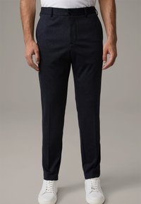 Granatowe, dopasowane spodnie z płaskim przodem, elastycznym paskiem w talii i bocznymi kieszeniami, zestawione z białymi trampkami. Gładka tekstura tkaniny.