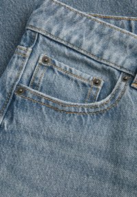 Κοντινή λήψη τσέπης από ανοιχτό μπλε τζιν με ορατές ραφές, τρούκ και κλασική υφή υφάσματος.