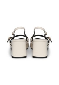 Sandales à talons avec un dessus lisse beige, des bretelles noires et un talon bloc. Brides de cheville réglables avec une fermeture à boucle en métal.