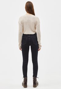 Beige ribbeltrui, zwarte skinny jeans met twee achterzakken en bruine veterschoenen. De outfit heeft een relaxte pasvorm en een gestructureerde stof.
