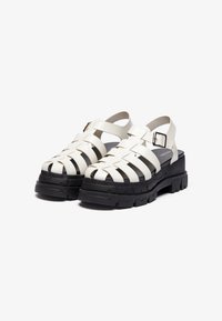 White strappy sandals with a chunky black platform sole. Features a buckle closure and a woven design on the upper.