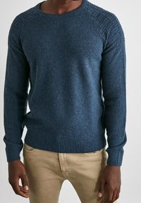 Mörkblå stickad tröja med texturerade axlar, ribbade manschetter och nederkant. Består av ett tjockt garn med ett subtilt mönster genom hela plagget.