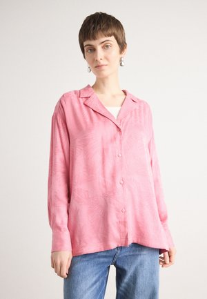 Camicia button-up rosa con una texture morbida, caratterizzata da un motivo a foglie, colletto, maniche lunghe e una vestibilità relaxed. Abbinata a jeans blu.