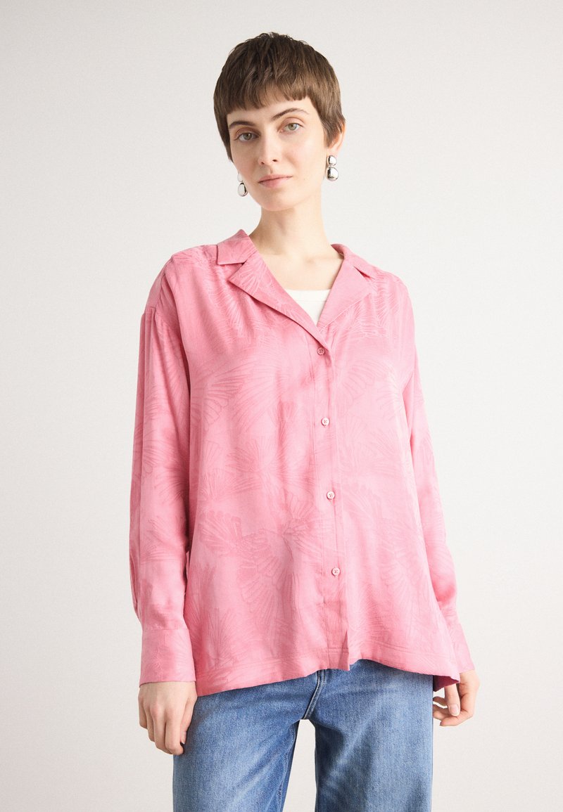 Pink button-up shirt with a soft texture, featuring a leaf pattern, a collar, long sleeves, and a relaxed fit. Paired with blue jeans.