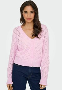 Cárdigan de punto rosa con cuello en V, que presenta un patrón de rombos, puños acanalados y cinco botones frontales. Combinado con jeans oscuros.