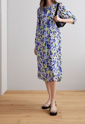 Robe à imprimé floral avec des nuances de bleu, de vert et de noir sur un fond violet clair. Manches longues, longueur genoux, avec une coupe décontractée.