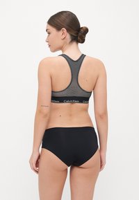 Stribet sports-bh i sort og hvid med racerback-design, der har en bred elastisk kant med "Calvin Klein" logo. Sorte trusser komplementerer sættet.