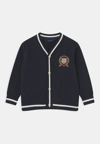 Námořnický svetr s bílými pruhy, ve tvaru V, se zapínáním na knoflíky. Obsahuje vyšitý emblém s vavřínem a štítovými detaily.