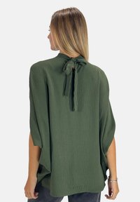 Grøn, tekstureret bluse med bindebånd ved halsen og vide ærmer, der har et flydende design og blødt stof.