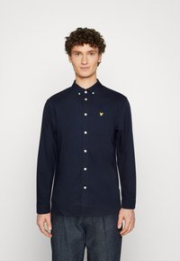 Camisa azul-marinho de manga longa com botões, bolso no peito, botões brancos e um pequeno logótipo amarelo bordado no lado esquerdo.