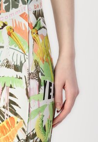 Detailný záber legín s živou, viacfarebnou tropickou potlačou so zvieratami a listami, vyrobených z hladkého, elastického materiálu.