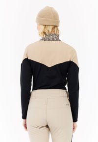 Sort og beige langærmet bluse med en mønstret krave, parret med beige bukser. Blusen har et zigzag-design over ryggen.