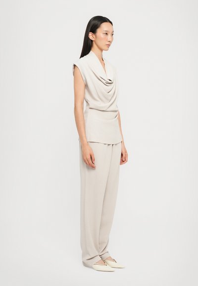 Beige Drapiertes Oberteil mit einem Cowl-Ausschnitt, kombiniert mit lockeren, passenden Hosen und minimalistischen Slippern. Geschmeidige Textur, lässige Passform.