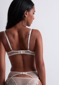 Ensemble de lingerie en dentelle beige avec des panneaux en mesh transparent, des bords festonnés, des bretelles réglables et une fermeture à crochets à l'arrière.
