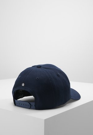 Granatowa czapka baseballowa z widocznymi przeszyciami i regulowanym paskiem typu snapback, umieszczona na białej powierzchni na tle gładkiego tła.