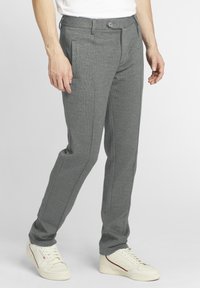 Pantalon gris texturé en matière douce avec une coupe ajustée, doté de poches latérales et d'une fermeture à bouton, associé à des baskets blanches.