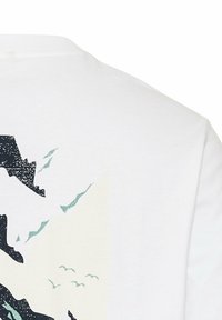 Witte katoen t-shirt met een zwart en teal grafisch ontwerp van vogels en gekartelde bergvormen op de achterkant. Zachte textuur, ronde hals.