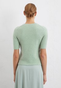 Maglione verde menta a maniche corte con una finitura testurizzata, scollatura e orlo a costine. Stile aderente con una texture liscia e morbida.