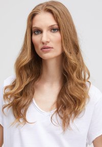 White V-neck t-shirt, lightweight fabric, featuring soft, loose fit. Model has long, wavy, light brown hair and neutral makeup.
