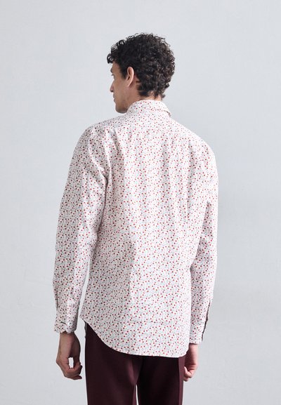 Long-sleeve shirt in white fabric with red and blue floral pattern. Features button cuffs and a rounded hem for a relaxed fit.