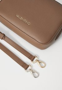 Bruine lederen tas met structuur, gouden hardware en het "Valentino" logo. Verstelbare banden zijn voorzien van metalen sluitingen. Glad, rechthoekig ontwerp.
