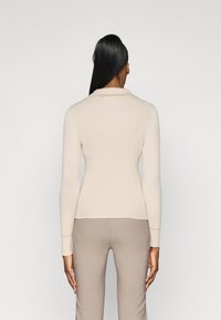 Ribbed beige pitkähihais t-paita, jossa on kaulus, suunniteltu istuvaksi, yhdistettynä vaaleanbeigeihin housuihin. Sujuva pinta ja viimeistelty ilme.